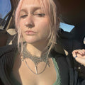 Person with pink hair and multiple necklaces sitting inside a vehicle.
